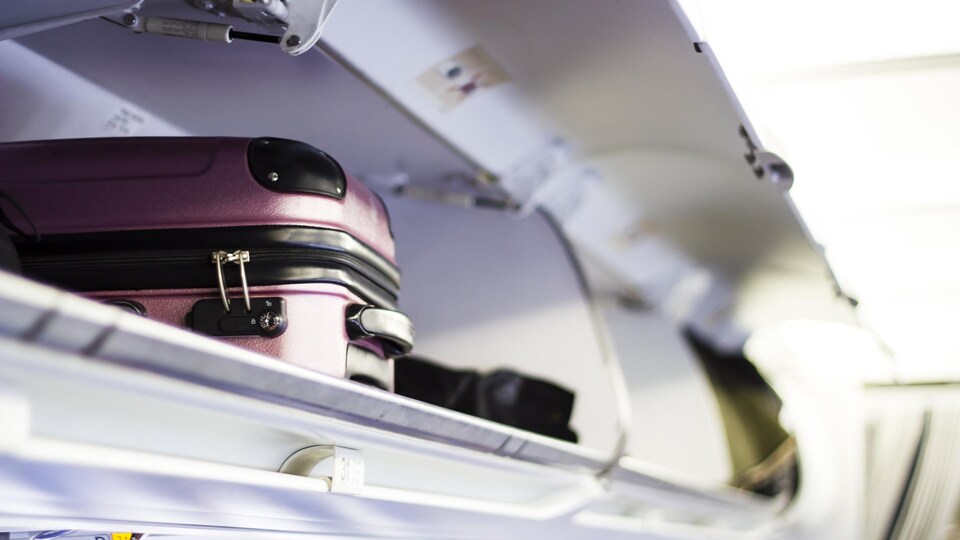 Une valise est posée dans le compartiment à bagage. Celui-ci est situé au-dessus des sièges des passagers. 