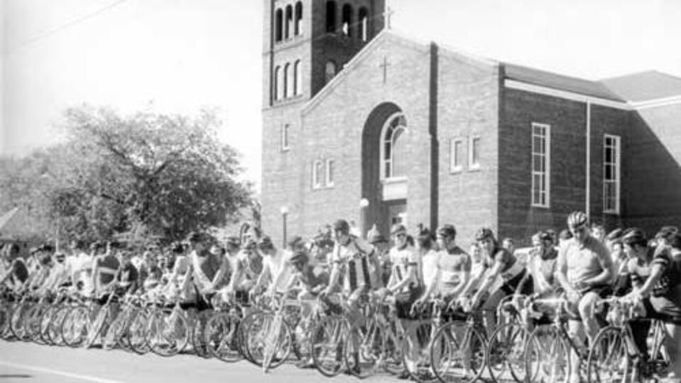 Photo noir et blanc de compétiteurs sur leurs bicyclettes à la ligne de départ d'une course.