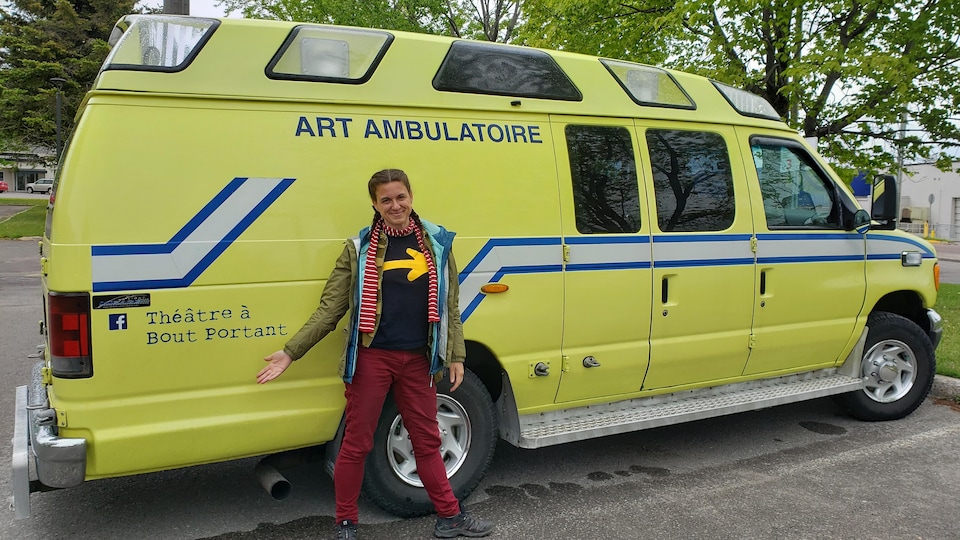 Vicky Côté, face à la caméra, présentant du revers de la main l'ambulance du spectacle Sortie de secours.