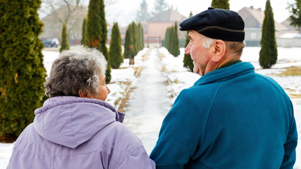 Un couple de personnes âgées marchant dans un sentier enneigé.