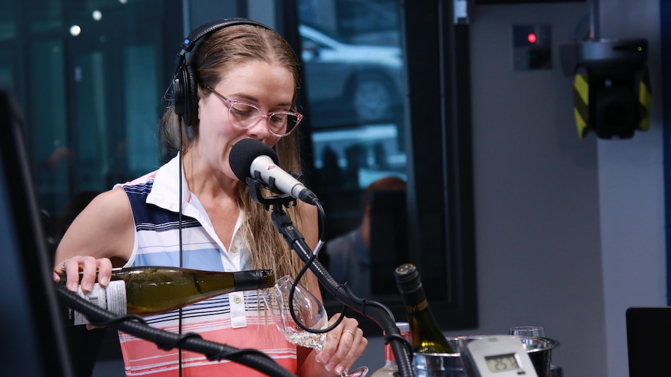 Une femme verse un verre de vin blanc dans un studio radio.