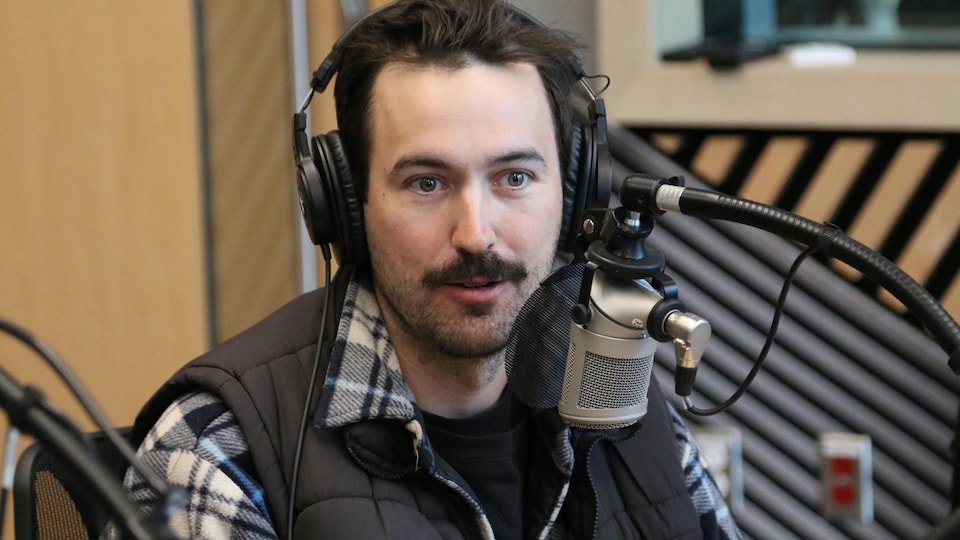 Un homme, casque d'écoute sur la tête, parle dans un micro lors d'une entrevue dans un studio de radio. 