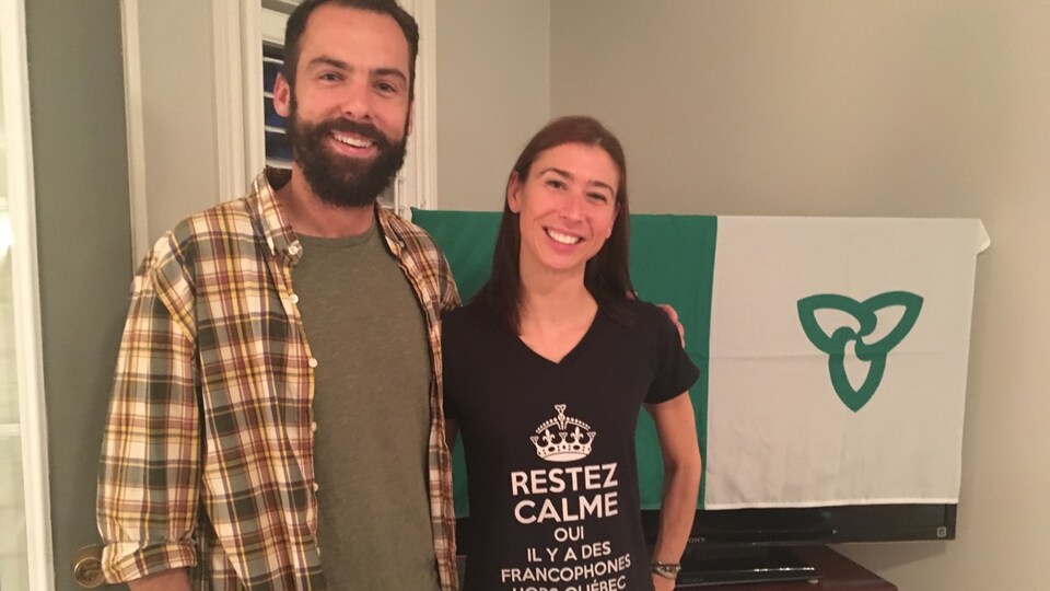 L'acteur et la chroniqueuse debout devant un drapeau franco-ontarien.