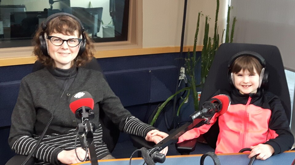 Une petite fille et sa mère sont assises devant des micros de Radio-Canada dans un studio.