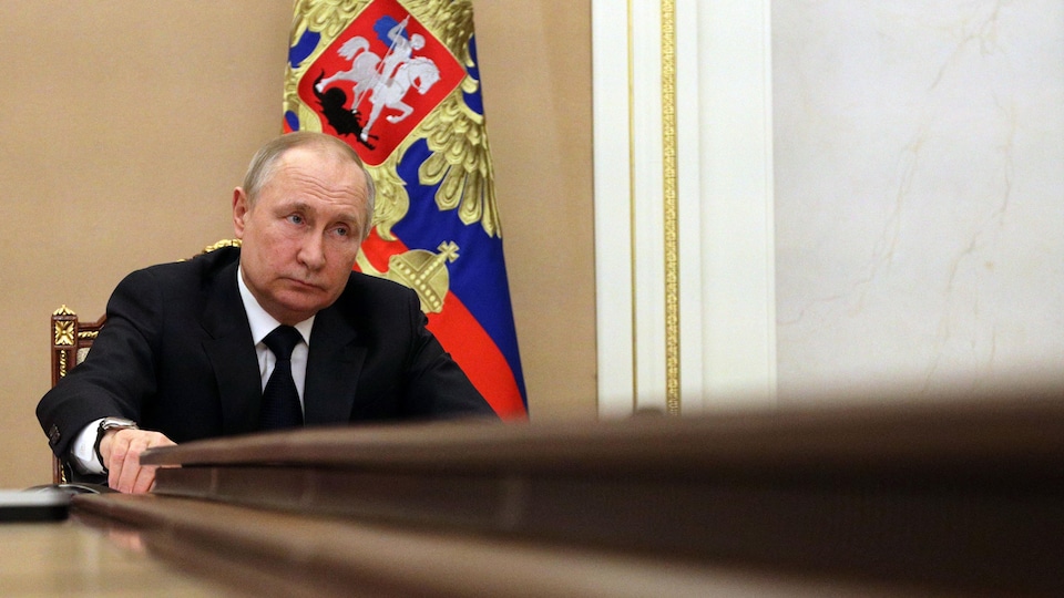 Le président russe Vladimir Poutine assis à une table. 
