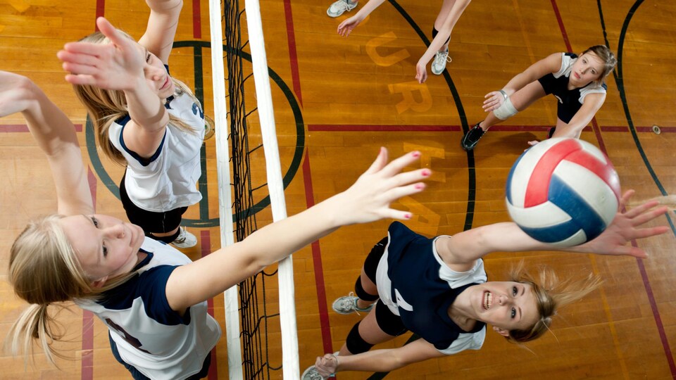 Des adolescentes en train de jouer au volleyball dans un gymnase.