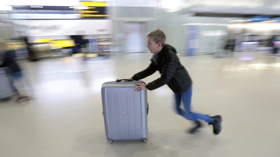 Un enfant pousse sa valise sur roues dans un aéroport.