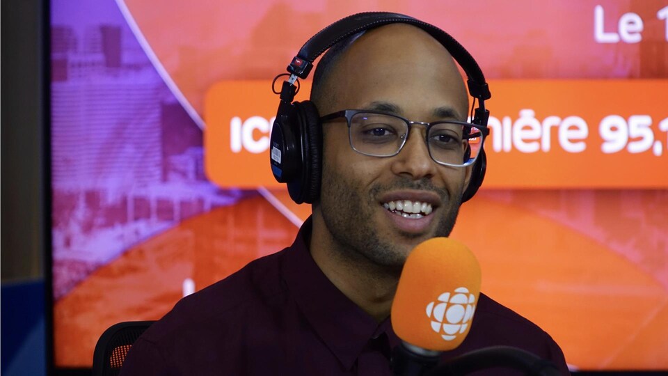 Webster derrière un micro dans un studio radio de Radio-Canada.