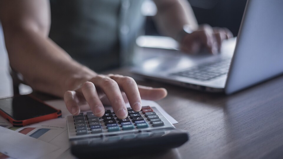 Un homme utilise une calculatrice et un ordinateur portable.