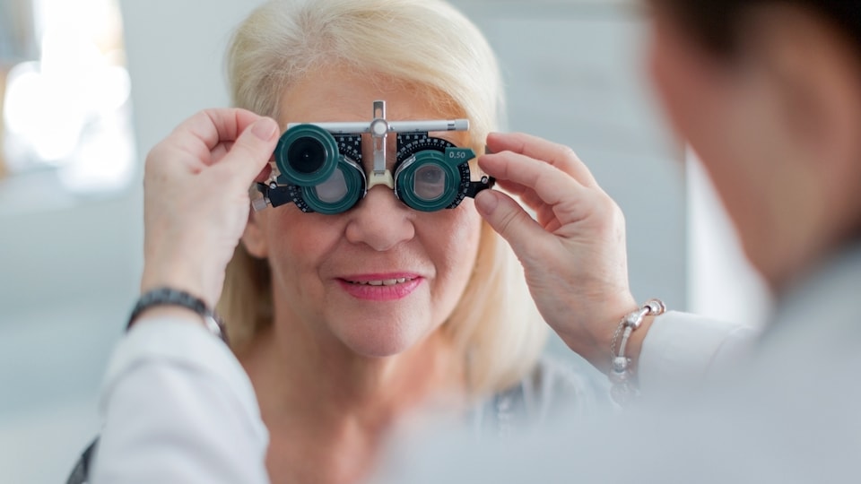 Une optométriste règle un appareil de mesure oculaire devant les yeux d'une patiente
