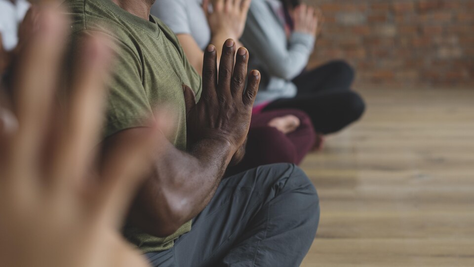 Un homme médite les jambes croisées et les mains jointes dans une classe de yoga. 