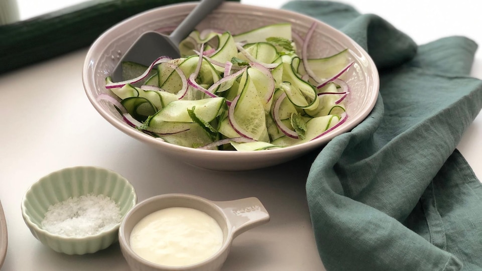 Un bol de salade de concombre en rubans avec un petit bol de vinaigrette à l'ail.