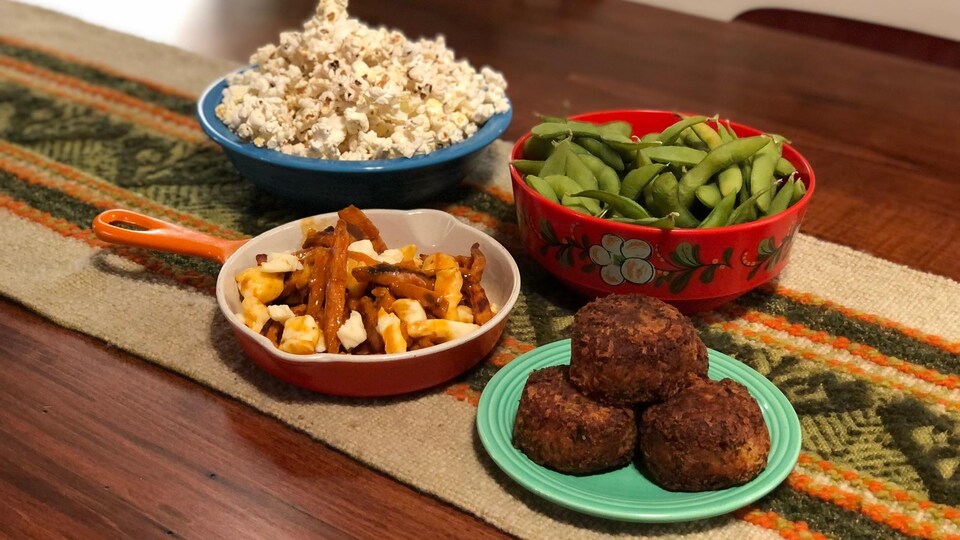 Un bol de maïs soufflé, un plat de poutine penjadbi, un bol d'edamame et une assiette de croquettes de crabe.