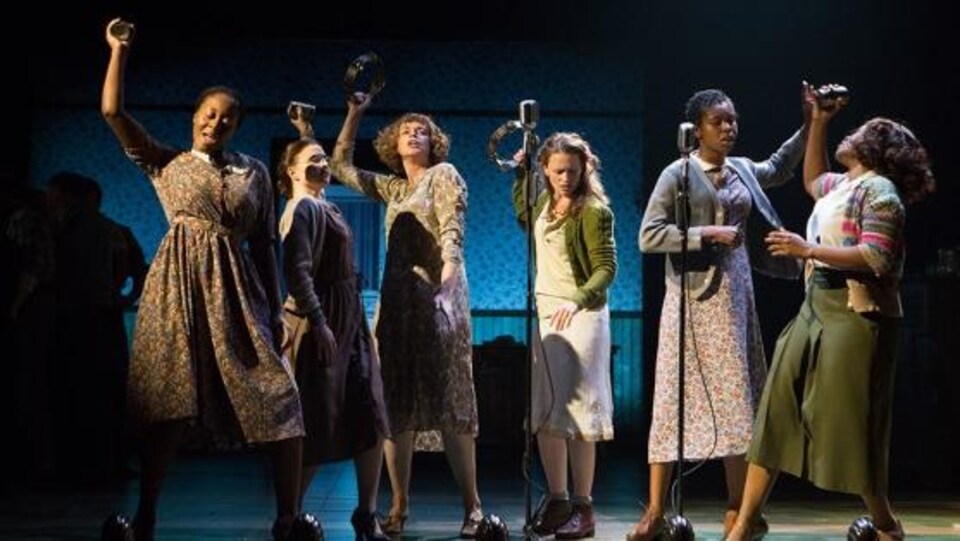 6 femmes chantent et dansent devant des microphones.