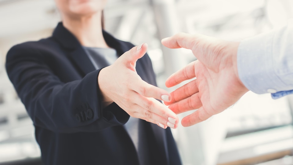 Une femme habillée en veston tend la main à un homme pour une poignée de main
