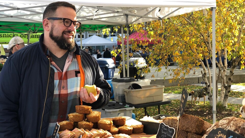 Simon A. Thibault regarde un comptoir de pâtisseries dans un marché extérieur.