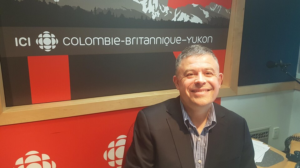Un homme dans aux cheveux courts sel et poivre qui est assis dans un studio de radio.