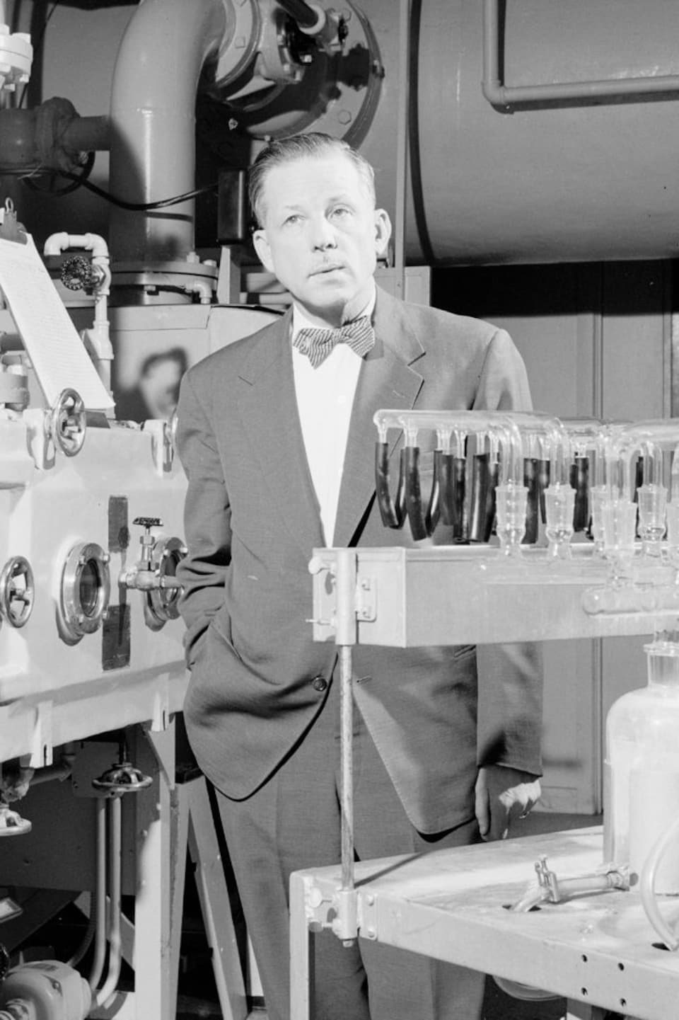 Le microbiologiste Armand Frappier se tient debout à côté d'équipements scientifiques.