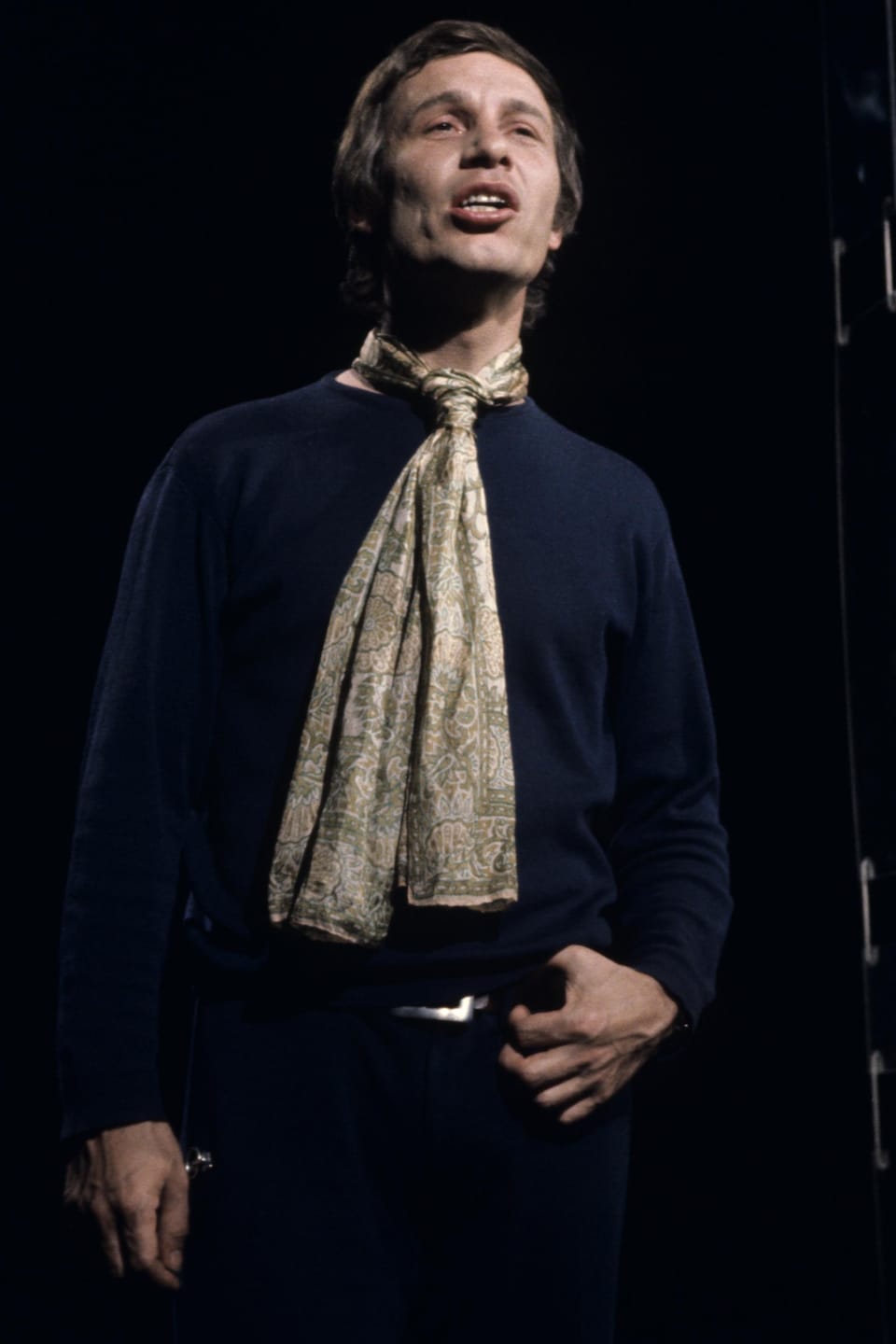 Jean-Pierre Ferland, vêtu d'un foulard, chante sur un plateau d'émission de télévision. 