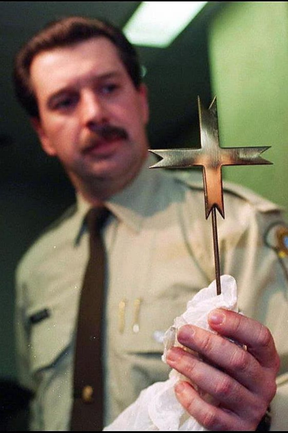 Gros plan sur une croix de métal tenue par un policier.