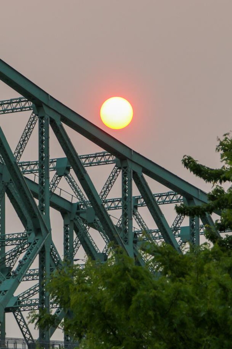 Une boule orangée surplombe le pont Jacques-Cartier sur un fond de ciel gris en raison de la fumée. 