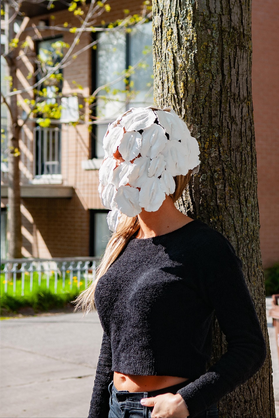 Une femme portant une masque formé de vulves est accotée sur un arbre par une journée ensoleillée à Montréal. 