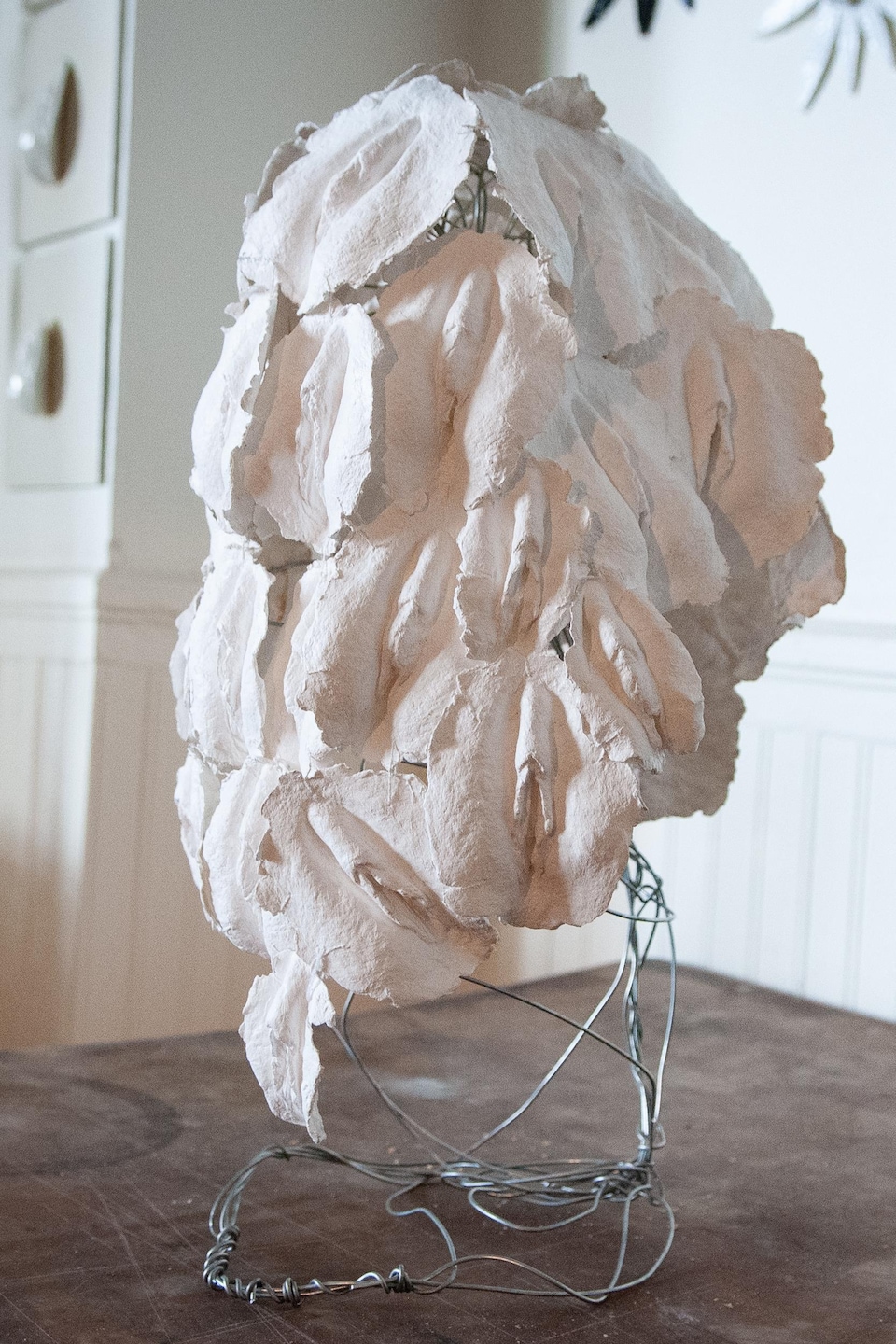 Un masque formé de petites vulves blanches attachées ensemble perché sur un support. 
