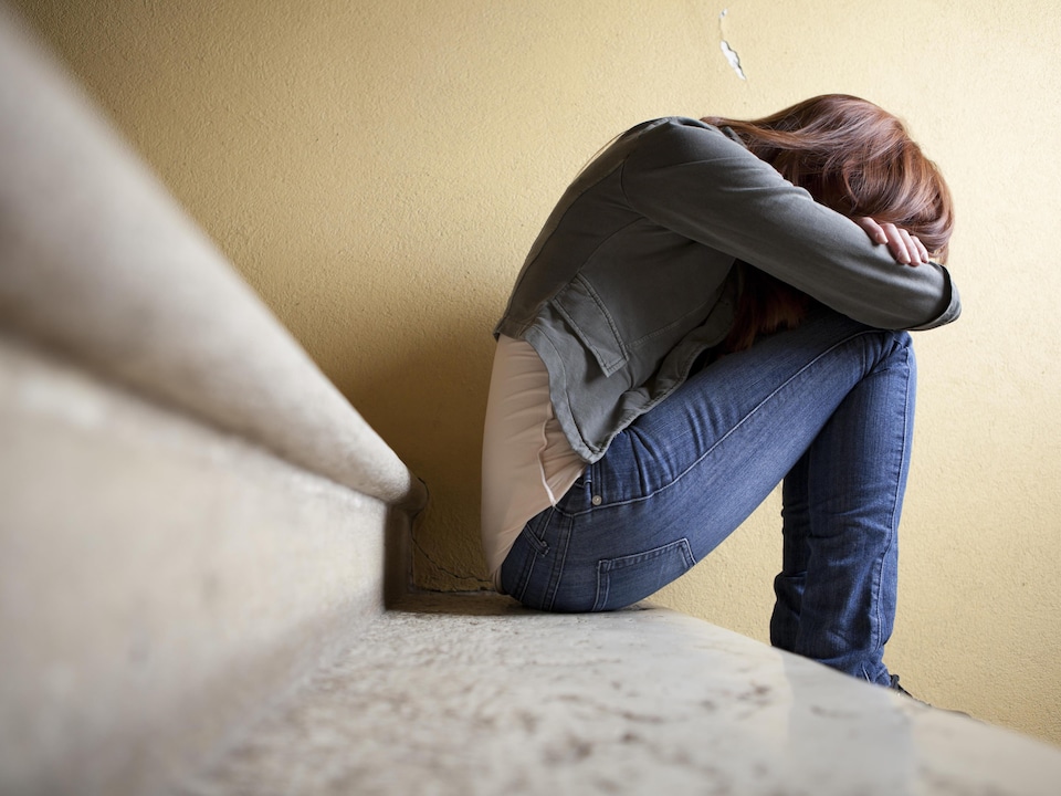 Une adolescente assise sur une marche d'escalier, la tête dans les bras.