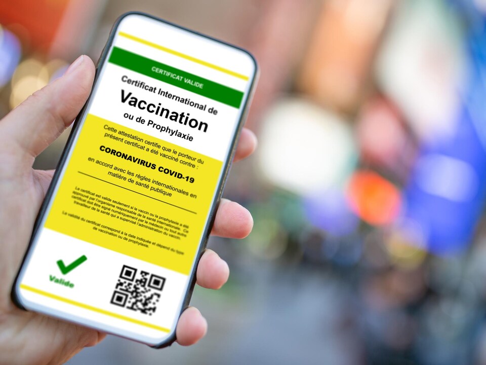 Gros plan sur une main tenant un téléphone avec une application attestant que le porteur du certificat a été vacciné contre la COVID-19.