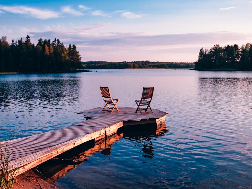 Deux chaises vides sur une plateforme flottante sur un lac au coucher du soleil.