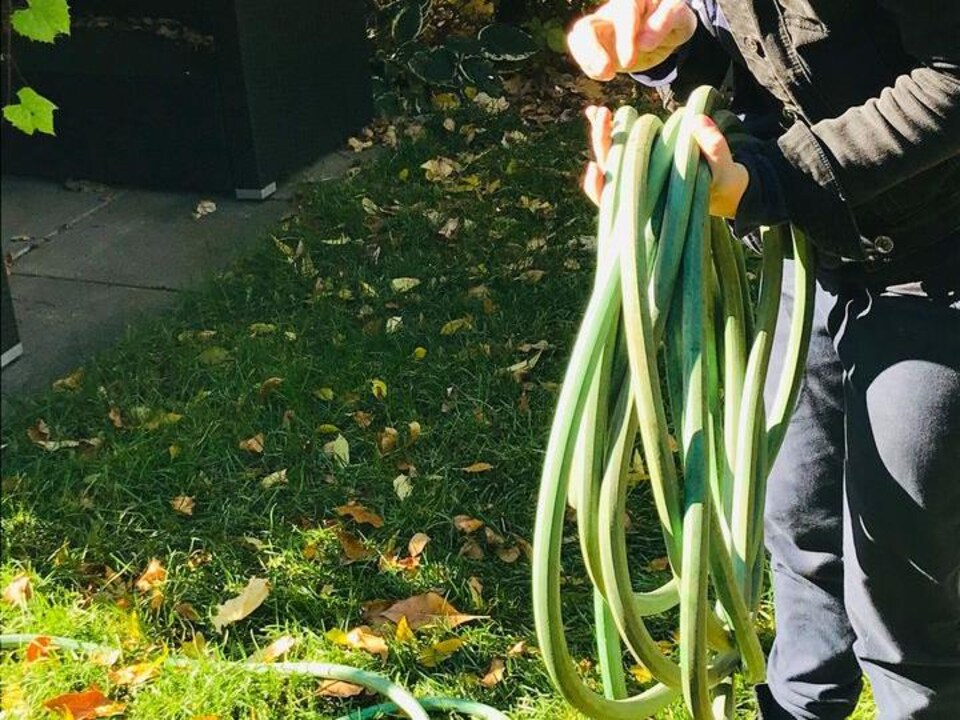 Une femme enroule son boyau d'arrosage. 