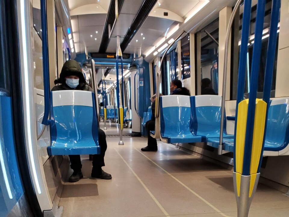 Deux personnes, dont une masquée, sont assises à bonne distance dans un wagon de métro vide.