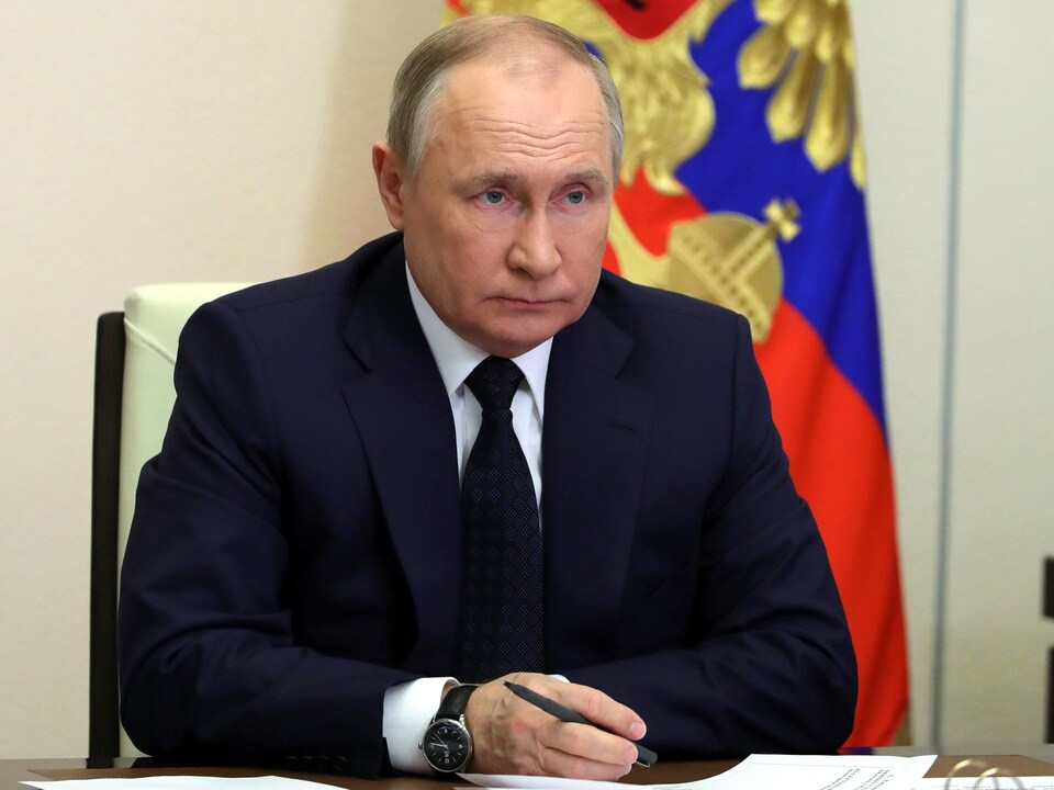 Vladimir Poutine, assis à une table, près d'un drapeau de la Russie. 