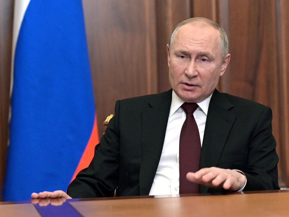 Vladimir Poutine assis à un bureau devant le drapeau russe.