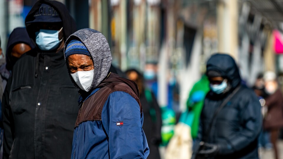 Des personnes portant un masque attendent en file sur un trottoir.