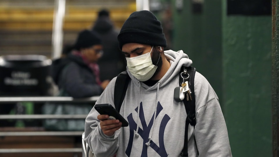 Un homme porte un masque chirurgical et consulte son téléphone mobile dans le métro de New York. 