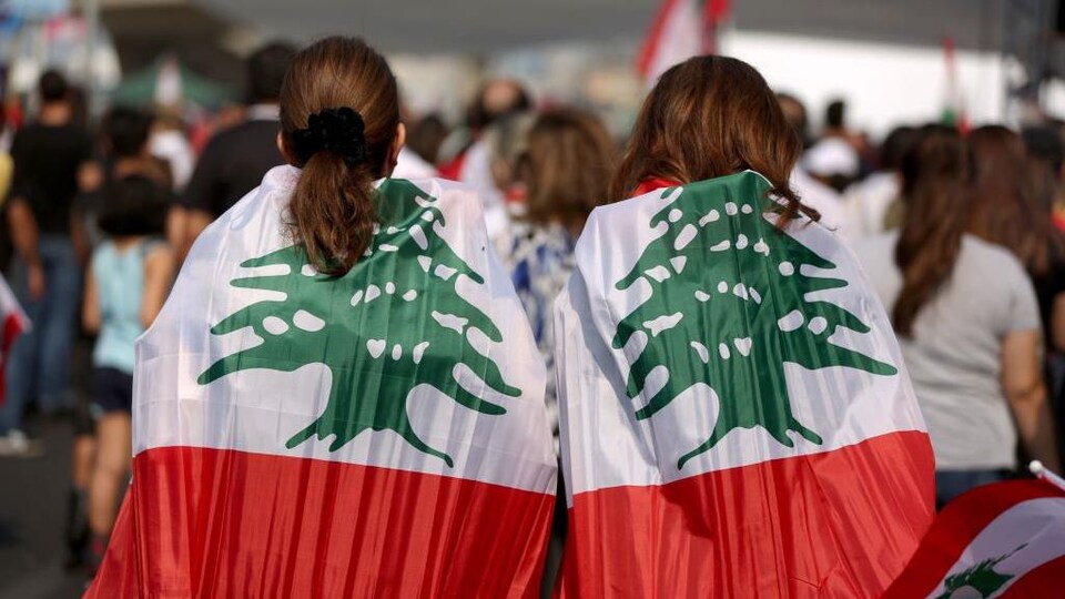 Deux femmes dans une foule sont habillées du drapeau du Liban. 