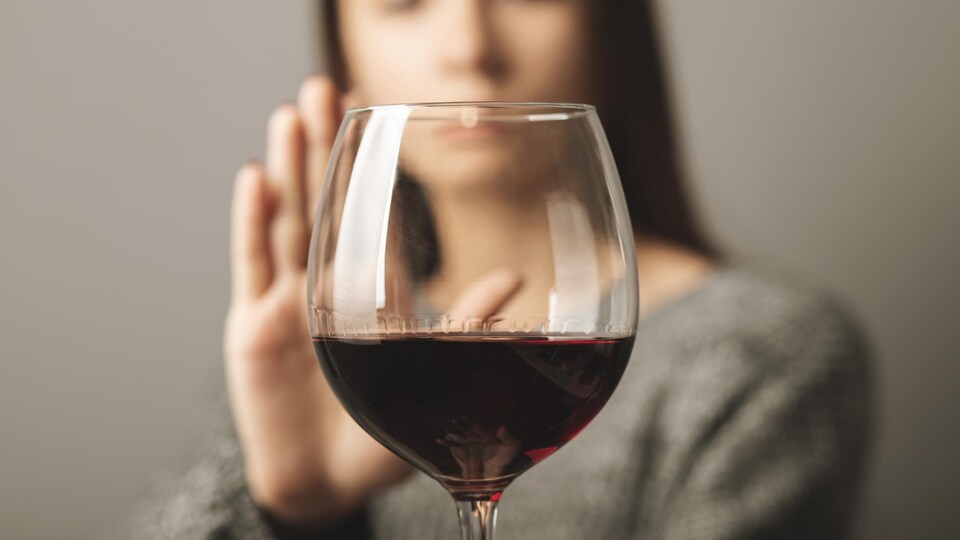 Une femme fait un signe d'arrêt de la main devant un verre de vin rouge.
