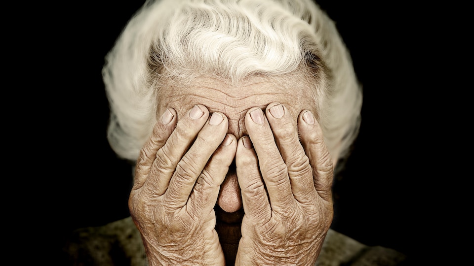 Une dame âgée se couvrant les yeux de ses mains.