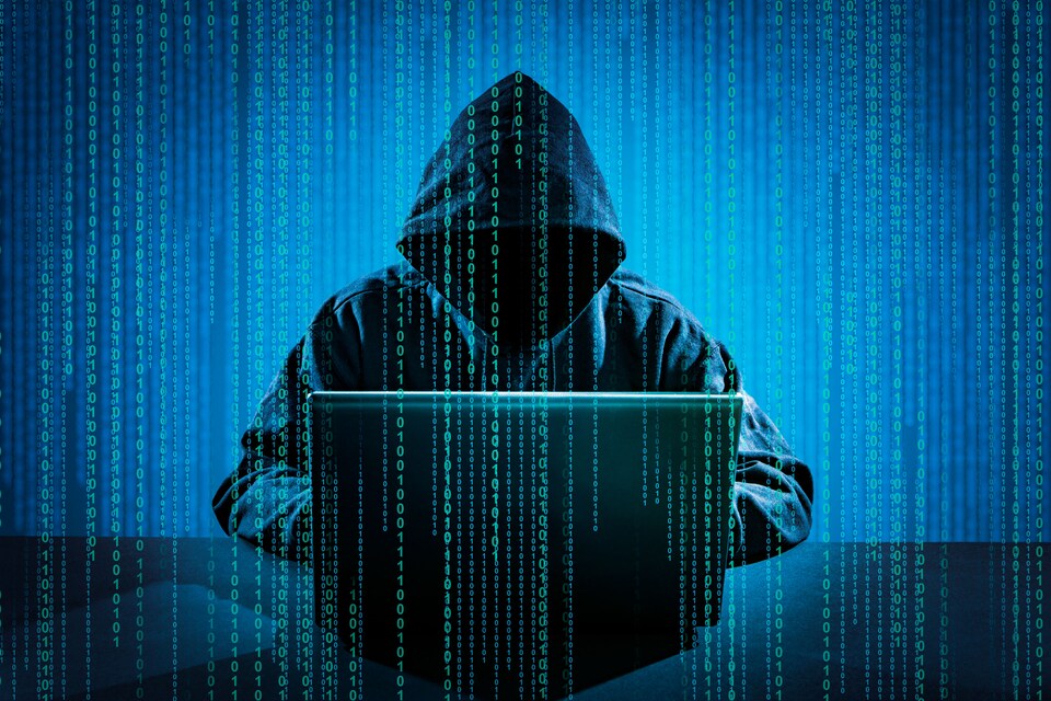 Une personne portant un capuchon travaille sur un ordinateur portable posé devant lui.