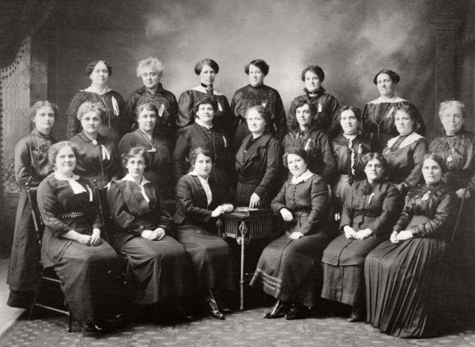 Photo ancienne en noir et blanc d'un groupe d'une vingtaine de femmes en vêtements d'époque.