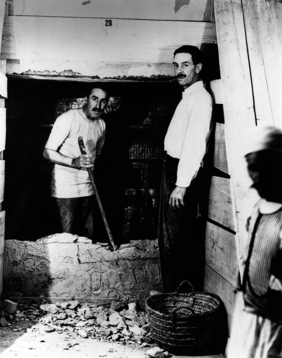 Photo en noir et blanc de deux hommes qui regardent la caméra. Ils font des travaux dans un lieu antique.