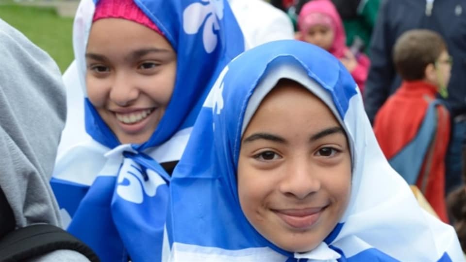 Photo d'immigrants. En surplomb, deux jeunes arborant le drapeau du Québec sur leur tête.