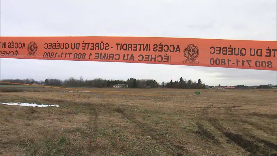 Un ruban orange de la Sûreté du Québec délimite un périmètre dans un champ.