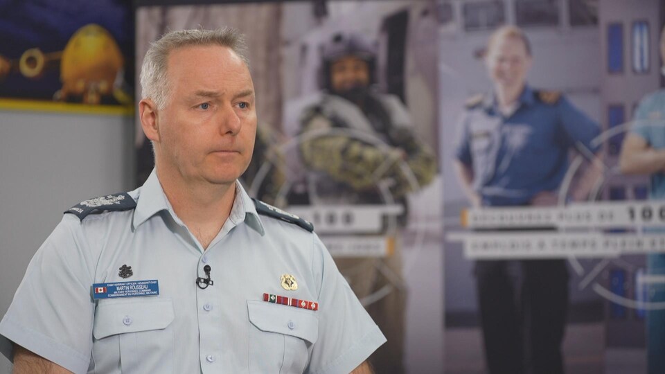 L'adjudant Martin Rousseau, porte-parole des Forces armées canadiennes assis devant des affiches publicitaires de l'armée