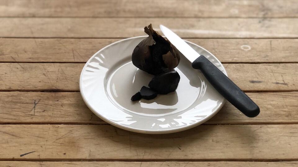Un bulbe d'ail noir dont une gousse a été écossée.
