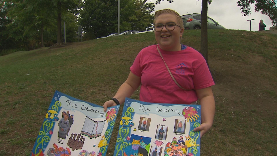 Une jeune fille présente un collage de photos et de dessins à la caméra.