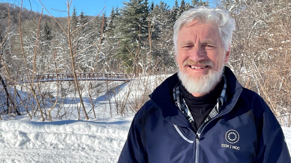Alain d'Entremont sourit à l'extérieur, en hiver. On reconnaît en arrière-plan la passerelle qui mène au sentier de la Sucrerie dans le parc de la Gatineau.