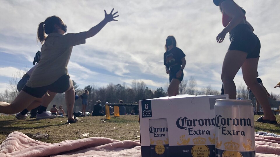 Un groupe de femmes joue au Spikeball, un jeu consistant à faire rebondir une balle sur un trampoline. Une caisse de bière Corona est installée en avant-plan. 