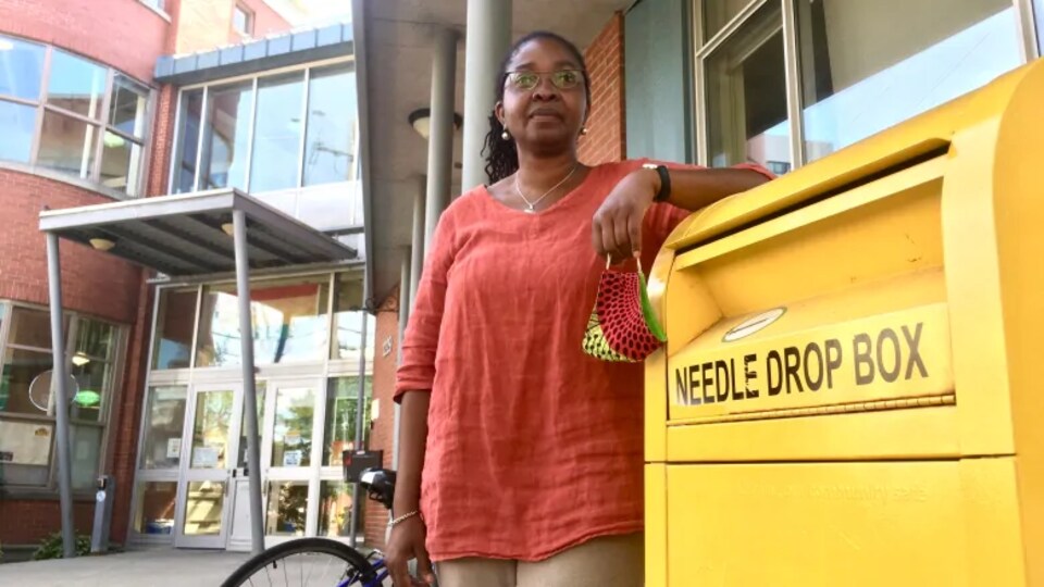 Angela Robertson devant son centre communautaire de santé, accoudée à une boîte de dépôt de seringues usagées.